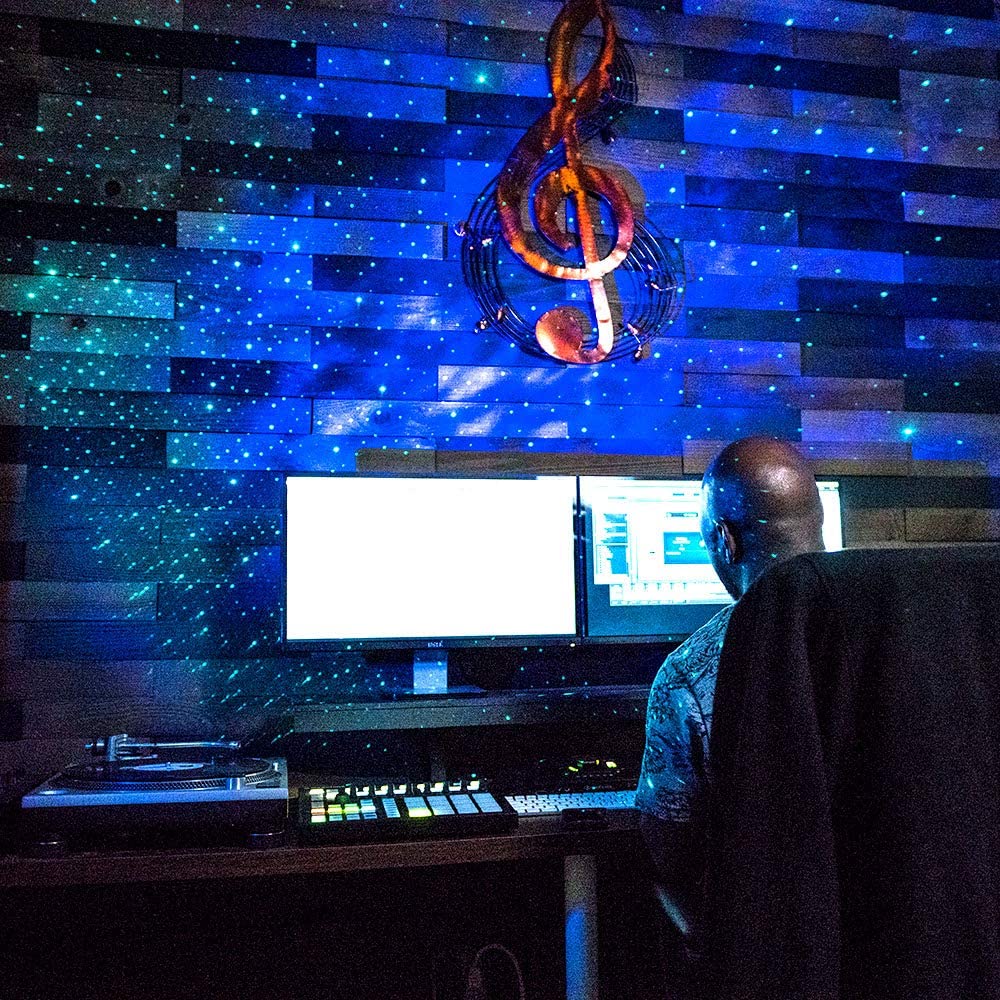 Person working at a computer with a decorative light fixture shaped like a treble clef on a blue and black wall.
