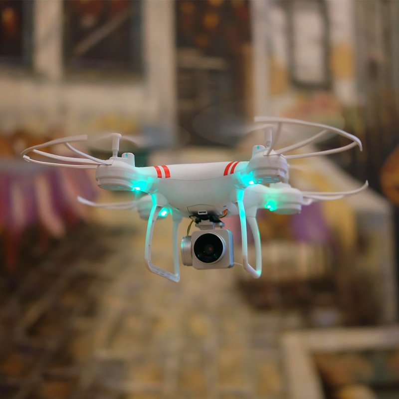 White drone with red accents flying in front of a blurred indoor background